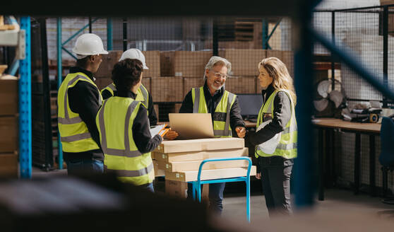 Lächelnde Lagerarbeiter bei einer Personalbesprechung mit ihrem Vorgesetzten. Eine Gruppe glücklicher Logistikmitarbeiter, die in einem großen Auslieferungslager als Team arbeiten. - JLPPF00446
