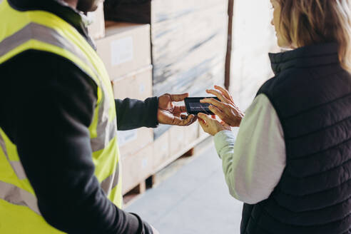Lagerverwalterin beim elektronischen Unterschreiben eines Verladebelegs auf einem Smartphone nach dem Empfang von Waren für den Versand. Spediteur, der eine Warenlieferung von einem Versender bestätigt. - JLPPF00449
