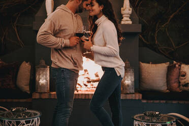 Affectionate young couple on a honeymoon. Two happy young lovers smiling while touching their faces together in a luxury hotel. Romantic young couple standing together and holding wine glasses. - JLPPF00493