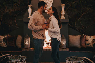 Young couple on a honeymoon vacation. Two happy young lovers smiling at each other affectionately in a luxury hotel. Romantic young couple standing together and holding wine glasses. - JLPPF00495
