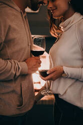 Junges Paar in einem romantischen Moment im Urlaub. Zwei liebevolle junge Liebende halten Weingläser, während sie in einem Luxushotel voreinander stehen. Junges Paar in den Flitterwochen. - JLPPF00497