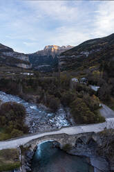 Erstaunliche Luftaufnahme einer Brücke unter einem wilden Fluss und kurvenreichen Straßen in einem malerischen Gebirgstal in der Stadt Torla in der Provinz Huesca - ADSF38791