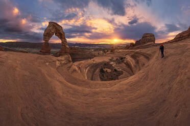 Reisefotograf fotografiert und bewundert die Landschaft der natürlichen Steinformation Delicate Arch in der trockenen Wüste gegen den bewölkten Himmel bei Sonnenuntergang im Arches National Park in Utah, USA - ADSF38800