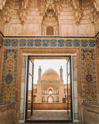 Shabby wall with ornamental elements and opened door against medieval mosque with dome and minarets located in Iran on summer day - ADSF38805