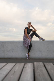 Reife Frau in Sportkleidung sitzt an der Wand vor dem Himmel - VPIF07414