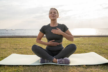 Mature woman doing breathing exercise on grass - VPIF07423