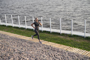 Mature woman jogging on footpath by sea - VPIF07432