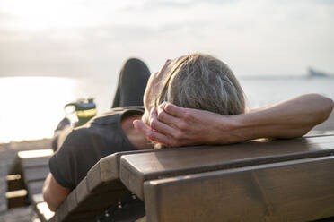 Ältere Frau entspannt sich auf einer Holzbank an einem sonnigen Tag - VPIF07438