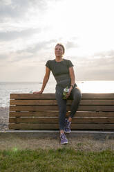 Smiling woman holding water bottle in front of bench - VPIF07440