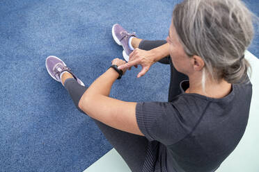 Mature woman checking time in smart watch sitting on exercise mat - VPIF07467