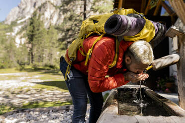 Wanderer mit Rucksack trinkt Wasser aus einem Brunnen - JCCMF07325
