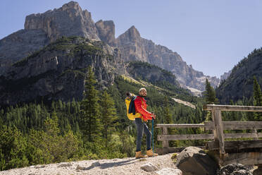 Hiker with backpack standing in front of Dolomites, Italy - JCCMF07328