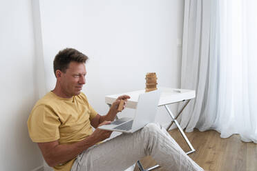 Smiling mature man showing toy block on video call through laptop at home - SVKF00548