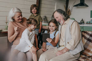 Glückliche Großeltern mit Kindern, die sich zu Hause einen Tablet-PC ansehen - YTF00120