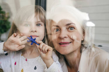 Nachdenkliche Großmutter und Enkelin mit Spielzeug, die aus dem Fenster schauen - YTF00130
