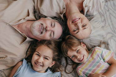 Happy grandparents and granddaughters lying together with heads in circle at home - YTF00136