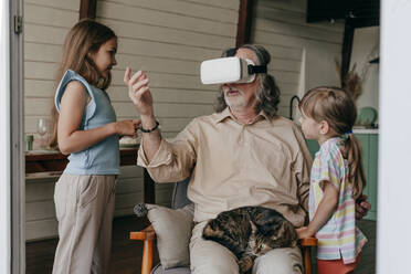 Großvater trägt Virtual-Reality-Simulator und gestikuliert mit seinen Enkeln zu Hause - YTF00139
