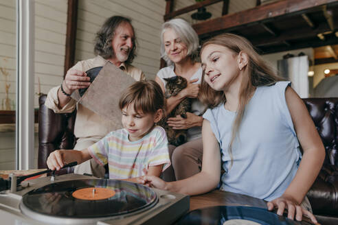 Grandchildren playing music on vinyl record player by grandparents at home - YTF00149