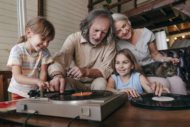 Großvater mit Enkeltöchtern, die zu Hause Musik auf einem Schallplattenspieler spielen - YTF00151