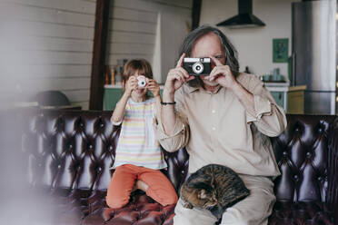 Großvater mit alter Kamera und Enkelin mit Spielzeugkamera beim Fotografieren zu Hause - YTF00156
