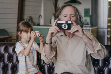 Enkelin mit Spielzeugkamera und Großvater mit alter Kamera beim Fotografieren zu Hause - YTF00157