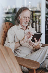 Älterer Mann sitzt auf einem Stuhl und benutzt einen Tablet-PC auf der Terrasse zu Hause - YTF00172