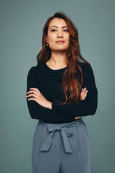 Self-confident young woman standing alone with her arms crossed. Strong independent young woman looking at the camera while standing against a studio background. Young woman embracing girl power. - JLPPF00510