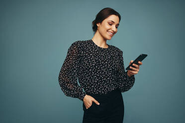 Selbstbewusste junge Frau, die fröhlich lächelt, während sie ein Smartphone benutzt. Junge Frau, die ein Mobiltelefon vor einem Studiohintergrund hält. - JLPPF00582