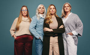 Empowered mature women standing together in a studio. Group of four mature women looking at the camera confidently while standing against a studio background. Independent women embracing girl power. - JLPPF00583