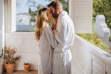 Leidenschaftliches Paar, das sich küsst, während es auf einem Balkon steht. Verliebtes Ehepaar, das einen schönen Morgen im Freien genießt. Romantisches Paar, das seinen Sommerurlaub in einem Luxushotel verbringt. - JLPPF00656