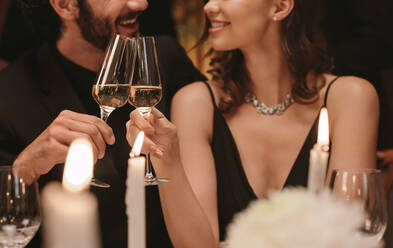 Junges Paar sitzt am Esstisch mit Kerzen und stößt mit Champagner an. Liebender Mann und Frau bei einer Gala-Dinner-Party. - JLPPF00661