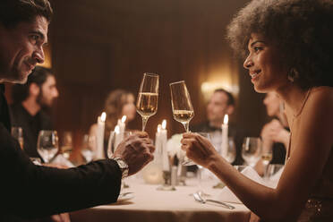 Paar stößt mit Champagner auf einer Dinnerparty an. Liebender Mann und Frau auf einer Gala-Dinnerparty, die mit Getränken feiern. - JLPPF00674