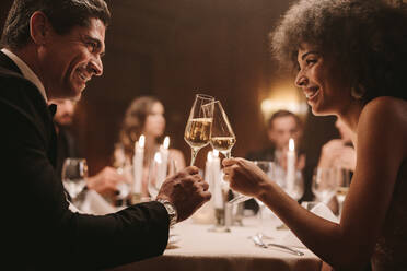 Ein Paar stößt bei einem Galadinner mit Champagner an. Freunde genießen auf einer Party einen Drink. - JLPPF00677