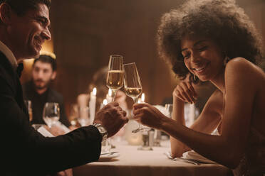 Verliebtes Paar auf einer Party, das mit Champagner anstößt. Mann und Frau sitzen am Esstisch auf einer Party und trinken. - JLPPF00678