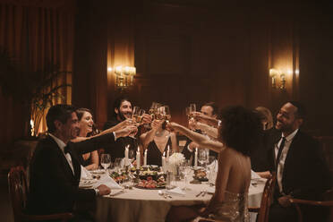 Eine Gruppe von Männern und Frauen feiert mit Wein bei einer Dinnerparty. Freunde genießen das Abendessen bei einer Galanacht. - JLPPF00685