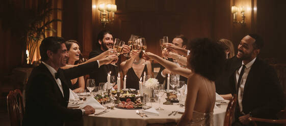 Eine Gruppe von Menschen stößt auf einer Gala-Party mit Getränken an. Gemischtrassige Freunde genießen eine Silvesterparty mit Getränken. - JLPPF00686