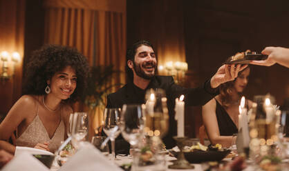 Eine Gruppe von Freunden bei einer Dinnerparty in einem Nachtclub. Multiethnische Männer und Frauen bei einem Gala-Dinner reichen sich gegenseitig warme Speisen. - JLPPF00689
