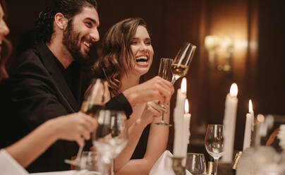 Junges Paar sitzt am Esstisch mit Kerzen und trinkt Wein. Gruppe von Prominenten bei einem Galadinner. - JLPPF00722