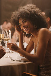 Attraktive afrikanische Frau stößt mit einem Freund auf einer Dinnerparty an. Eine Frau feiert mit Getränken bei einem Gala-Dinner. - JLPPF00727