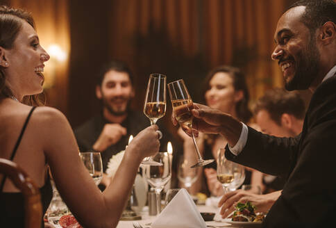 Multirassische Freunde auf einer Dinnerparty stoßen mit Weingläsern an. Fokus auf Mann und Frau, die auf ihre Getränke anstoßen, während sie auf einer Dinnerparty sitzen. - JLPPF00738