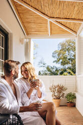 Ein Ehepaar, das sich morgens auf einem Hotelbalkon entspannt. Ein glückliches Ehepaar, das sich bei einem Kaffee gegenseitig anlächelt. Ein Paar, das einen romantischen Ausflug in einem Luxushotel genießt. - JLPPF00781