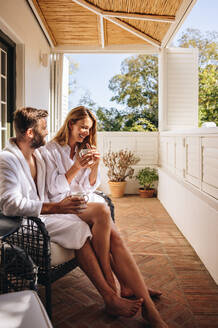 Glückliches Paar, das im Sommer zusammen Urlaub macht. Lächelndes Paar, das sich auf einem Balkon entspannt und Kaffee trinkt. Verheiratetes Paar, das einen romantischen Wochenendausflug in einem Luxushotel genießt. - JLPPF00783
