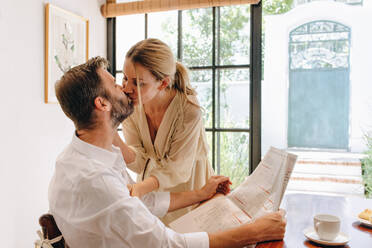 Romantic couple kissing at a tea table inside a hotel. Affectionate couple enjoying a lovely morning together in the summer. Married couple spending a weekend getaway in a luxury hotel. - JLPPF00809