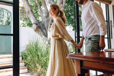 Cheerful couple going outdoors together. Happy married couple holding hands while leaving a hotel dining area. Smiling couple enjoying a lovely morning during their summer vacation. - JLPPF00815