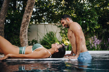 Vergnügtes Paar an einem luxuriösen Swimmingpool. Glückliches junges Paar, das sich in einem Spa-Resort am Pool entspannt. Junges Paar, das während seiner Flitterwochen viel Zeit miteinander verbringt. - JLPPF00855