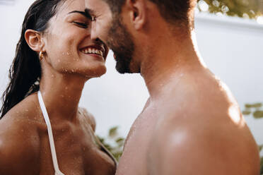 Glückliches junges Paar, das sich unter einer Dusche im Freien küsst. Romantisches junges Paar, das lächelt, während es in einem Luxus-Spa-Resort zusammen duscht. Glückliches Paar, das sich während seiner Flitterwochen zusammenfindet. - JLPPF00870