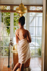 Young woman going for a luxury bath at a hotel. Rearview of an attractive young woman standing in front of a bathtub in a white bath towel. Glamorous young woman enjoying a vacation at a luxury hotel. - JLPPF00886