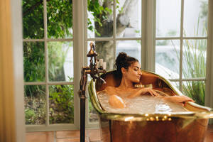 Entspannendes Bad in einem Luxus-Spa-Resort. Attraktive junge Frau, die ihren Körper in einer Badewanne wäscht. Glamouröse junge brünette Frau, die sich während eines Wochenendausflugs in einem Spa-Resort entspannt. - JLPPF00894