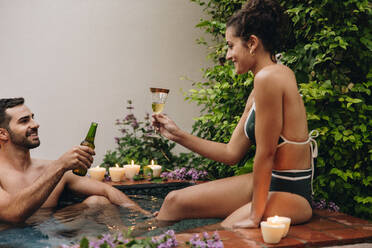 Lovers making a toast in a plunge pool. Two happy young lovers enjoying alcoholic beverages while relaxing in a luxury plunge pool. Young couple being romantic during their honeymoon vacation. - JLPPF00905