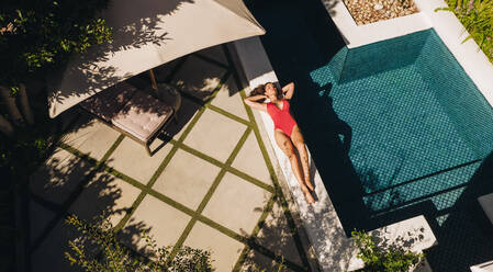 Sonnenbaden im Sommer. Blick von oben auf eine attraktive junge Frau, die sich in einem roten Badeanzug am Rande eines Swimmingpools entspannt. Junge Frau, die einen Wochenendausflug in einem Luxus-Spa-Resort genießt. - JLPPF00914